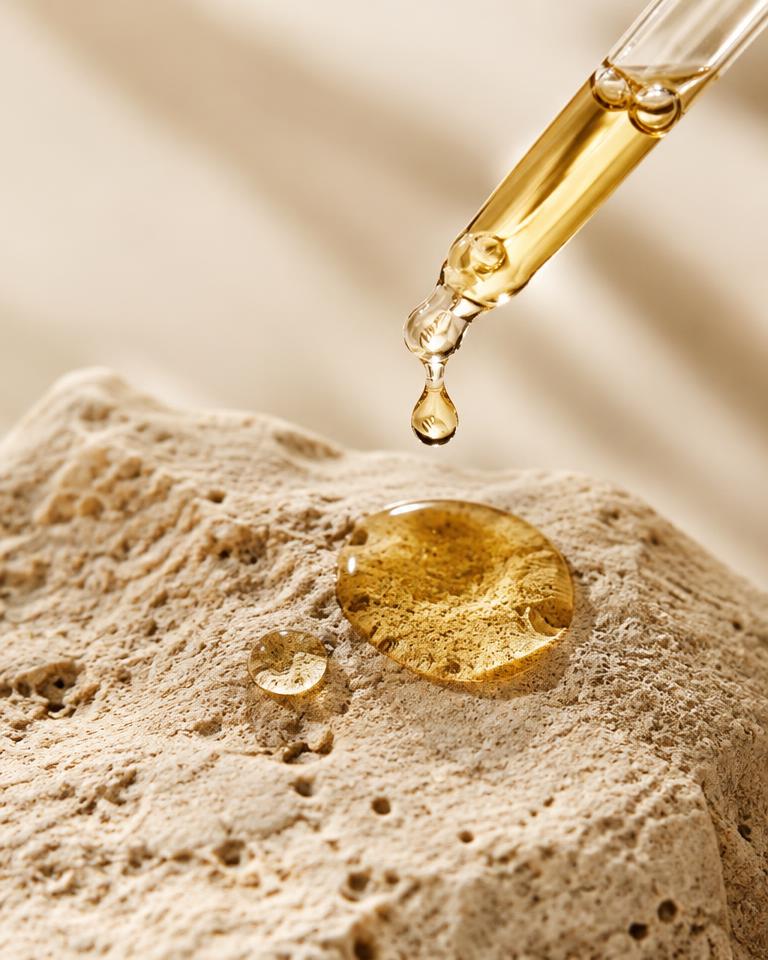 Golden serum drop falling onto stone